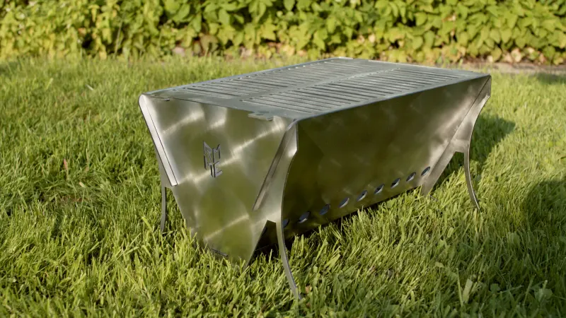Der fertige Schlitzer im Gras bei Abendsonne: Steckgrill aus Edelstahl mit geschlitzter Grillfläche, ME-Emblem in der Stirnseite